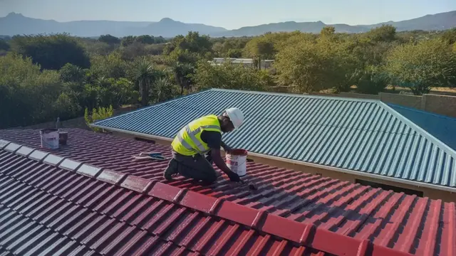 Painter in a hi-vis vest applying red coating to a tiled roof