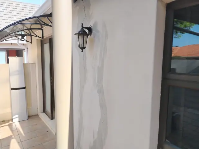 Exterior wall with a vertical crack filled with grey filler beside a wall lamp