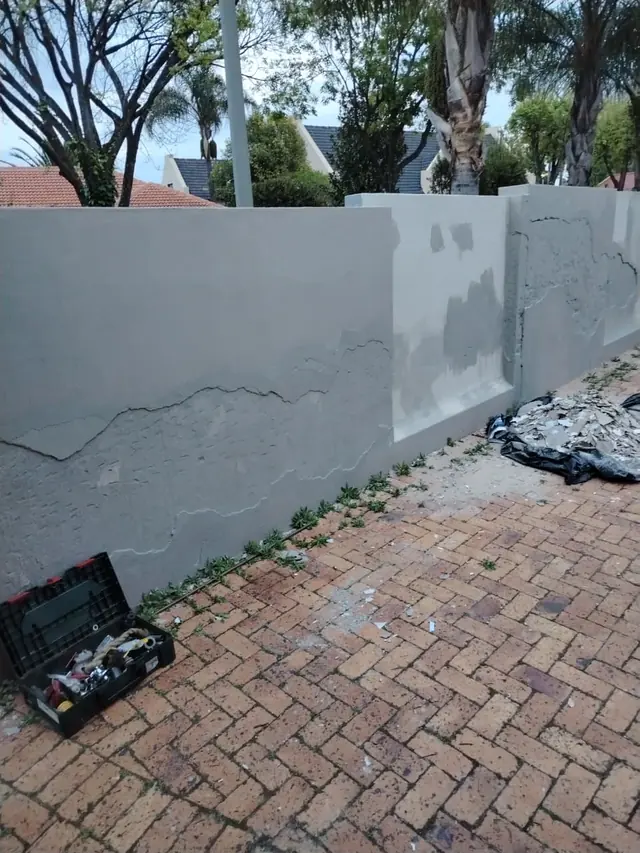 Boundary wall with cracked plaster being repaired and a toolbox on the brick paving