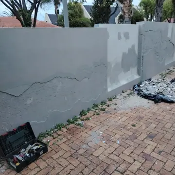 Boundary wall with cracked plaster being repaired and a toolbox on the brick paving