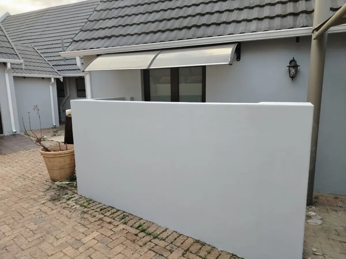 Freshly painted pale grey boundary wall in front of a tiled roof with a clear awning