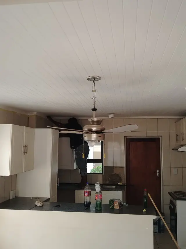 Kitchen with a white painted plank ceiling and a painter working above the cabinets