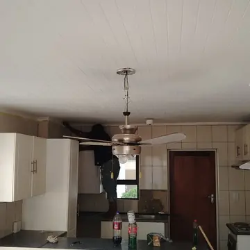 Kitchen with a white painted plank ceiling and a painter working above the cabinets