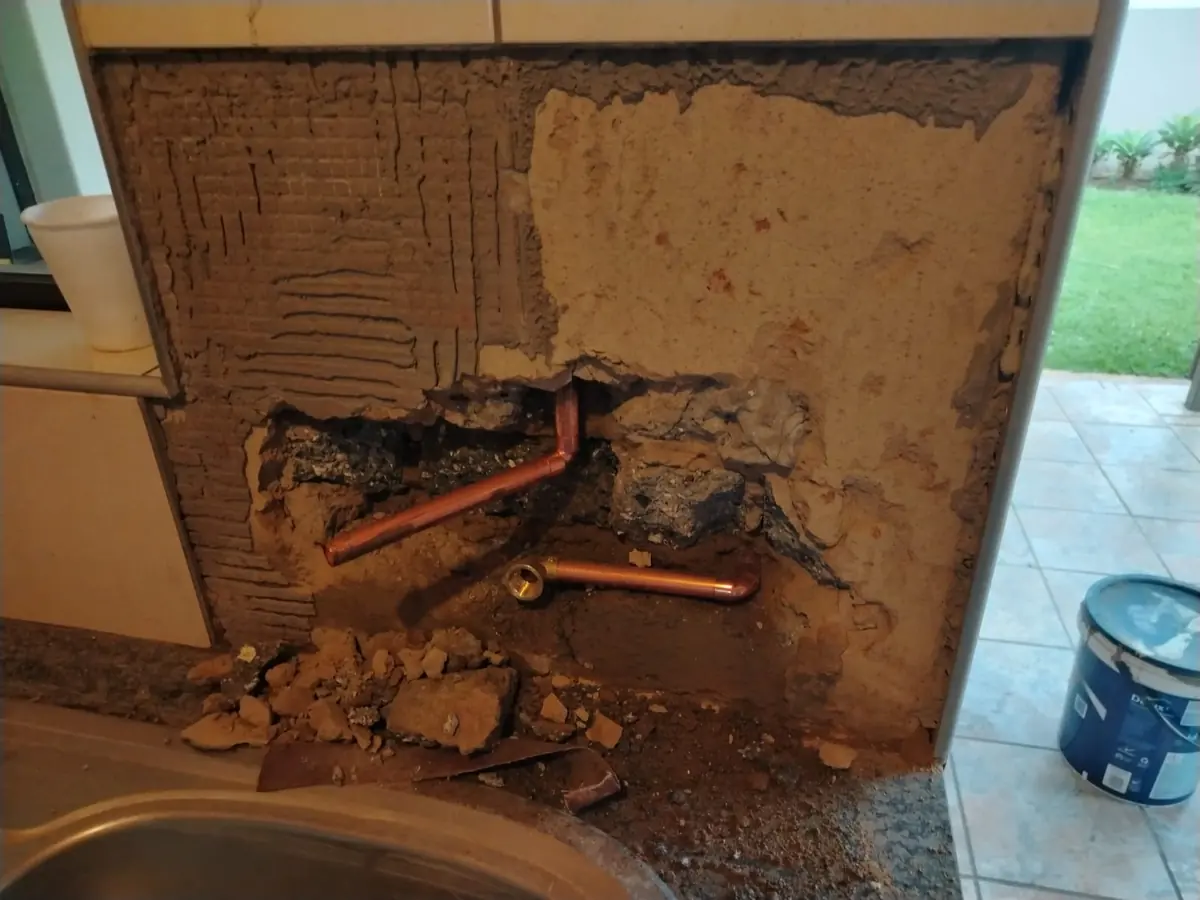 Wall behind a kitchen counter chiselled open to expose new copper plumbing pipes beside the sink