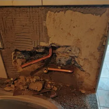 Wall behind a kitchen counter chiselled open to expose new copper plumbing pipes beside the sink