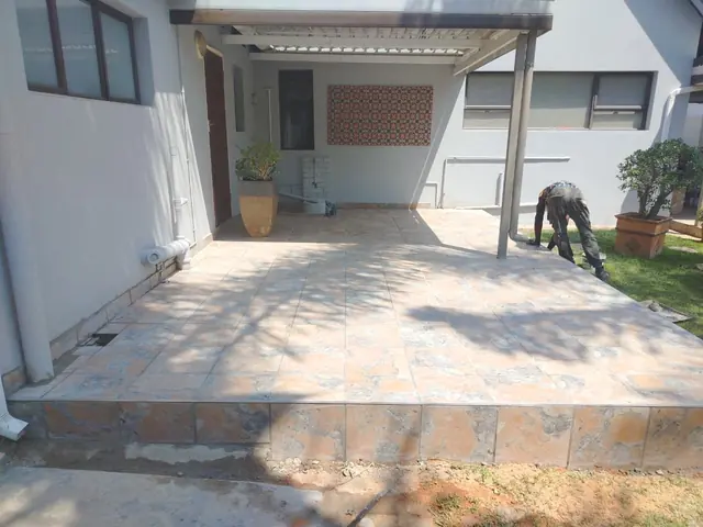 Worker laying tiles on a patio beside freshly painted grey walls