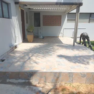Worker laying tiles on a patio beside freshly painted grey walls