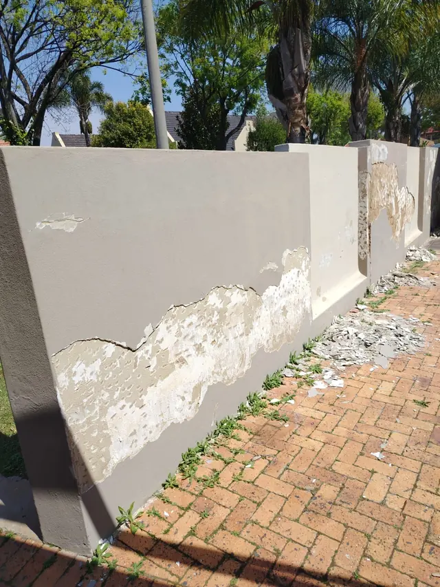 Boundary wall with large areas of peeling paint and plaster beside a brick-paved pavement