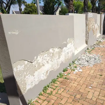 Boundary wall with large areas of peeling paint and plaster beside a brick-paved pavement
