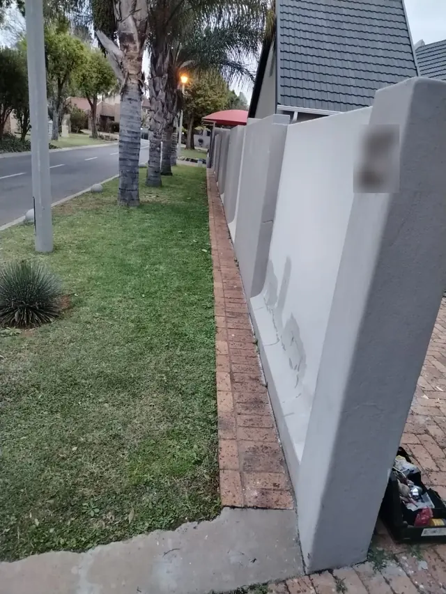 Grey primed boundary wall with filled repairs beside a lawn and palm trees