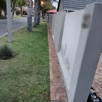 Grey primed boundary wall with filled repairs beside a lawn and palm trees