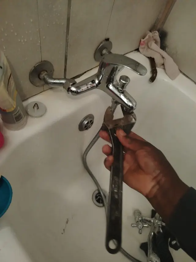 Hand holding an adjustable wrench on a bath mixer tap being replaced