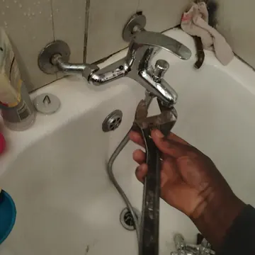 Hand holding an adjustable wrench on a bath mixer tap being replaced
