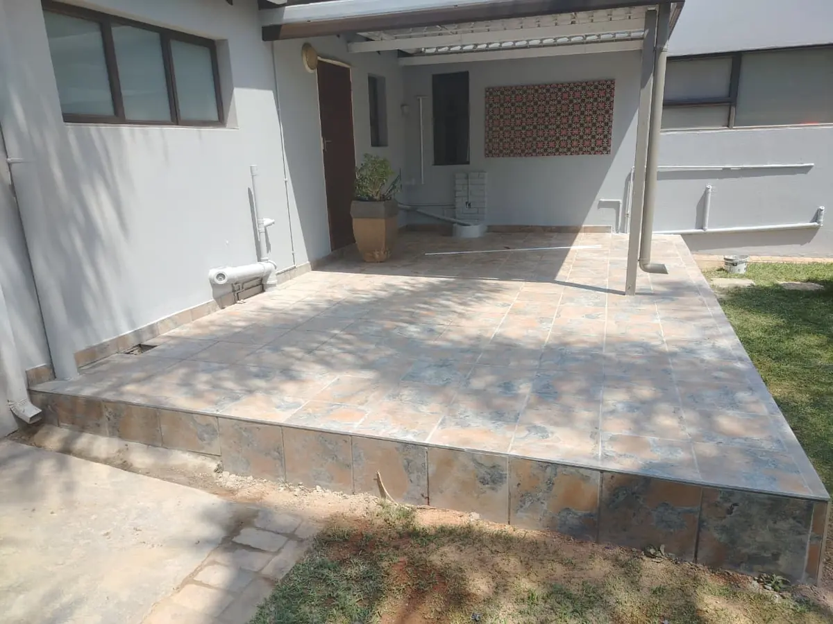 Raised tiled patio under a covered veranda beside grey painted walls