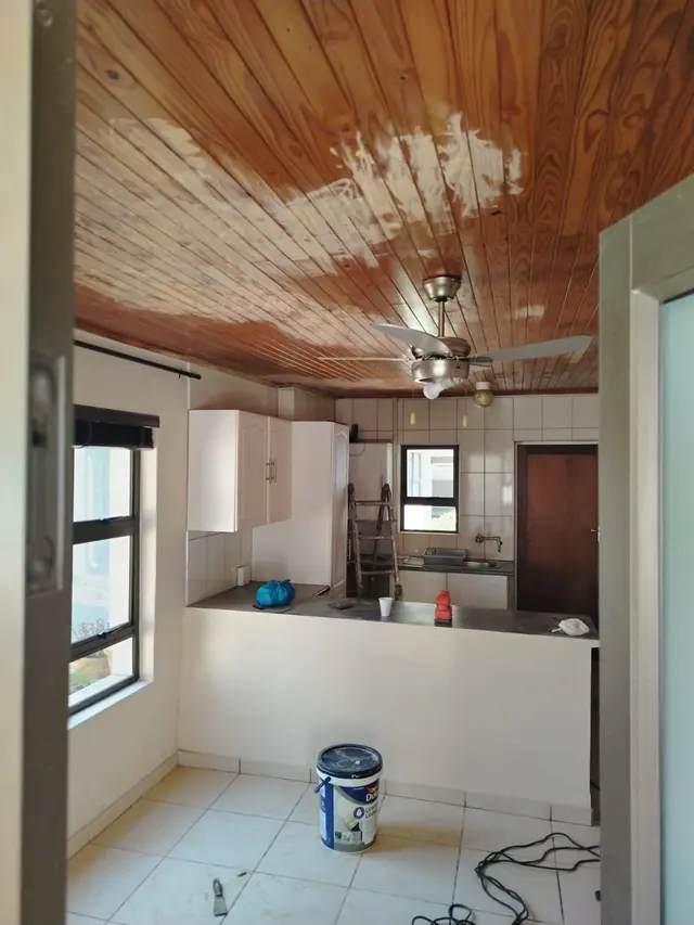 Kitchen with a timber plank ceiling partly stripped and a tin of paint on the floor