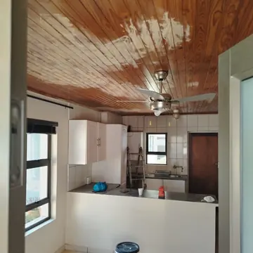 Kitchen with a timber plank ceiling partly stripped and a tin of paint on the floor