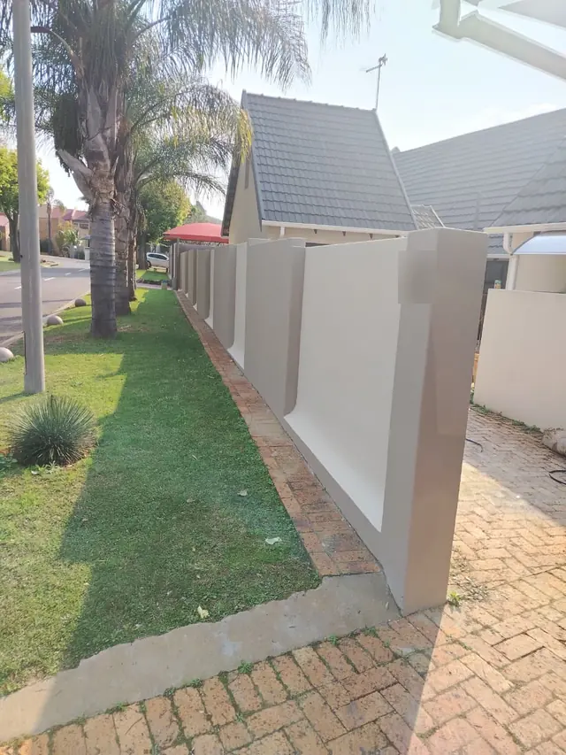Freshly painted two-tone cream and taupe boundary wall beside a lawn and brick paving