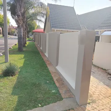 Freshly painted two-tone cream and taupe boundary wall beside a lawn and brick paving