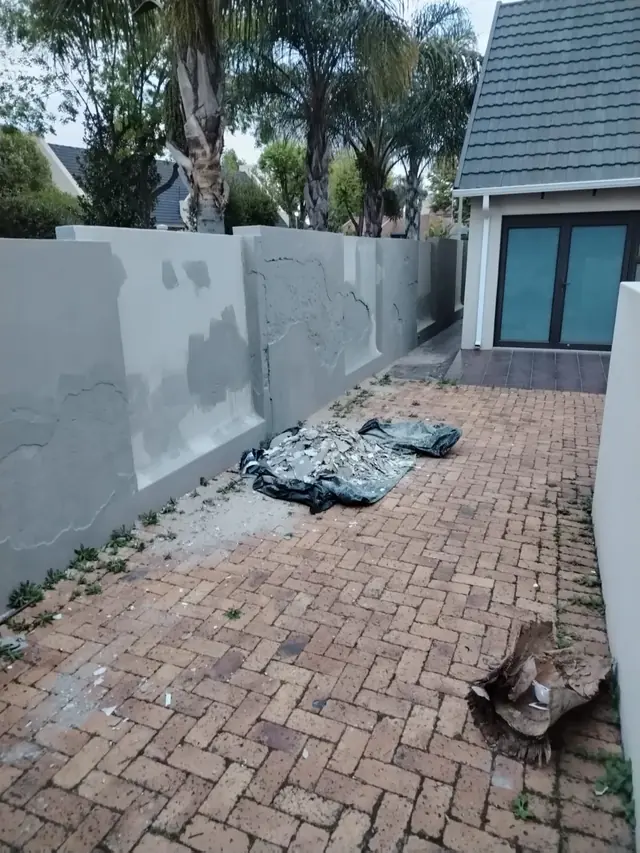 Courtyard wall with grey primer, filler repairs and removed plaster piled on a tarp