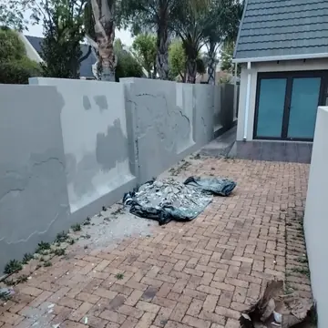 Courtyard wall with grey primer, filler repairs and removed plaster piled on a tarp