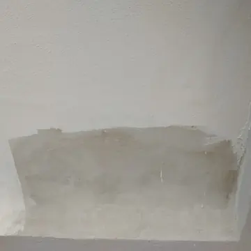 White textured wall with a rectangular patch sanded back to bare plaster